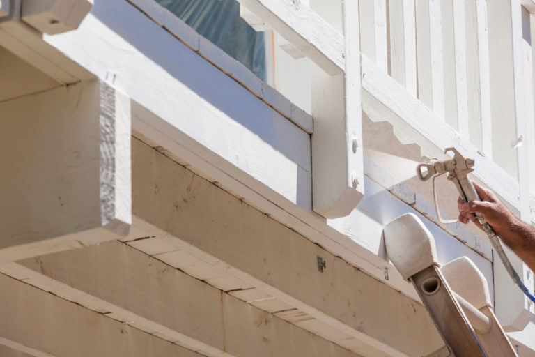 House Painter Wearing Facial Protection Spray Painting A Deck of A Home.